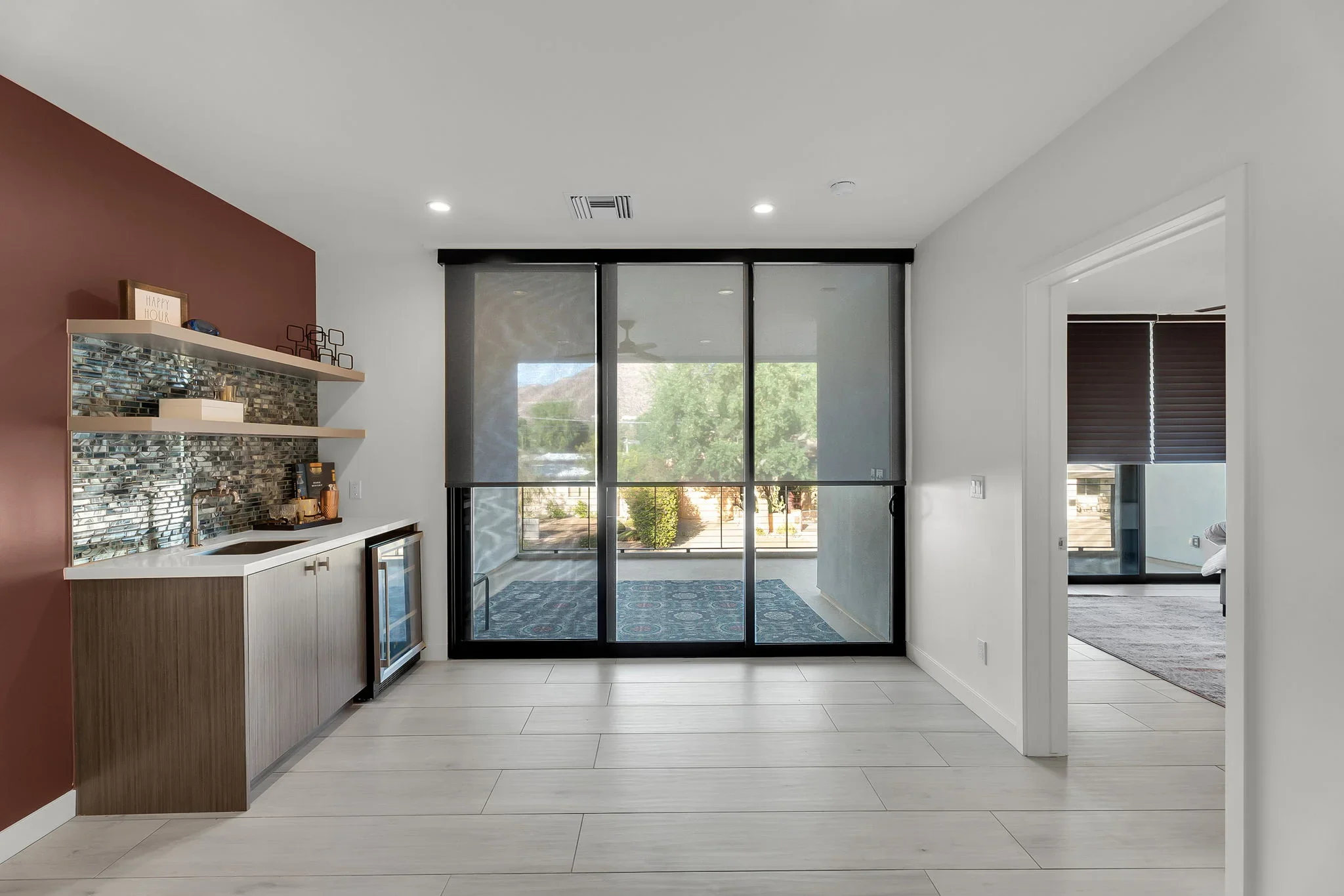 Modern interior with black sliding glass doors, burgundy accent wall, stone backsplash, and light tile flooring