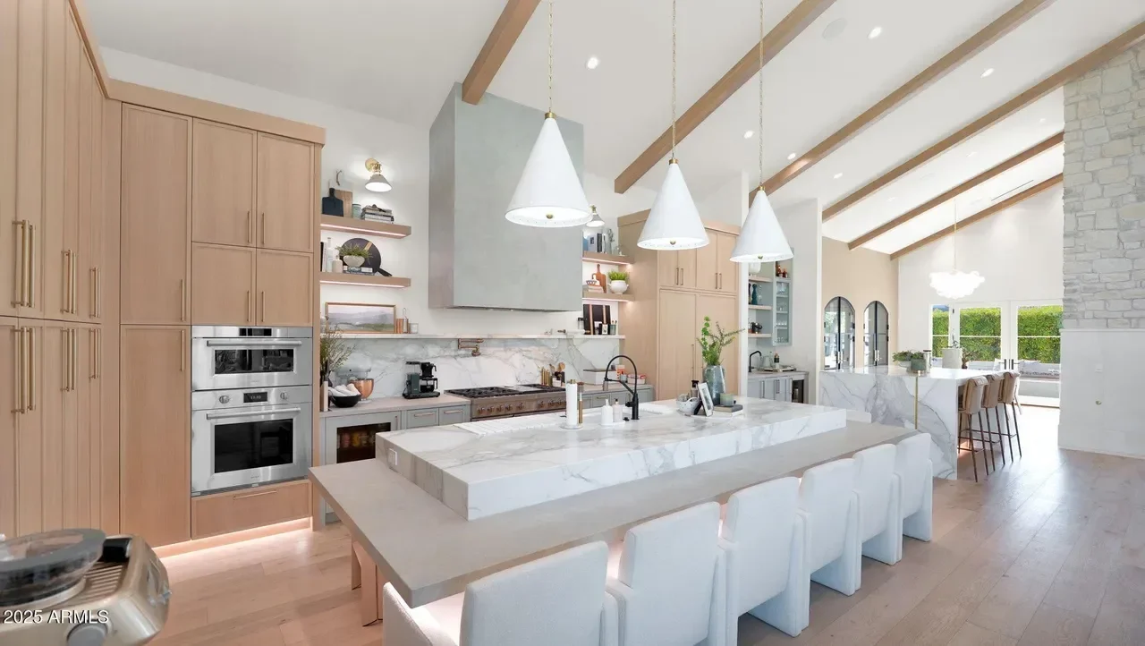 Modern kitchen with light wood cabinets, marble countertops, stainless steel appliances, and exposed wood beams