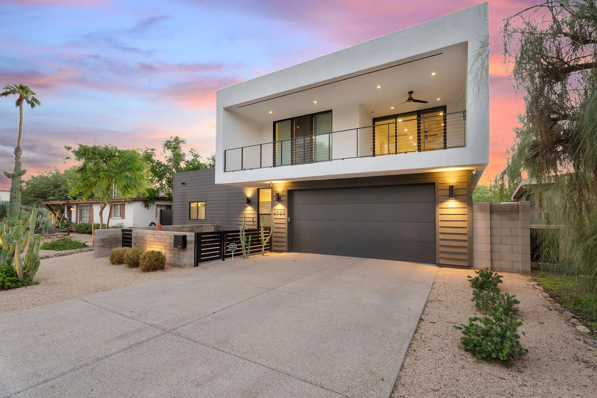 Modern two-story home with white stucco and dark siding, concrete driveway, and desert landscaping