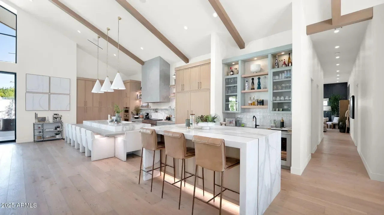 Modern kitchen with marble island, wood cabinetry, exposed beams, and open shelving