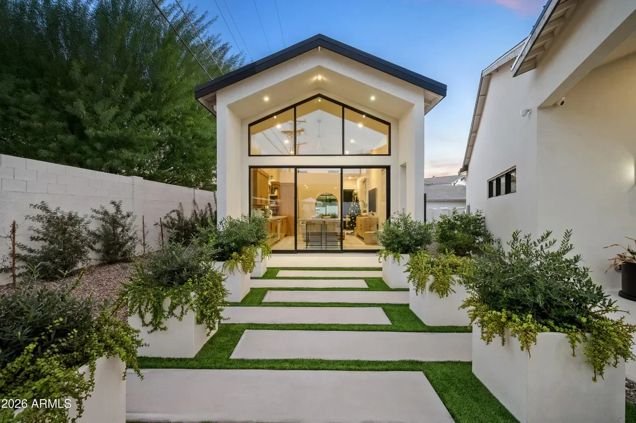 Modern white stucco home addition with black-framed glass doors and windows, concrete and grass courtyard entry