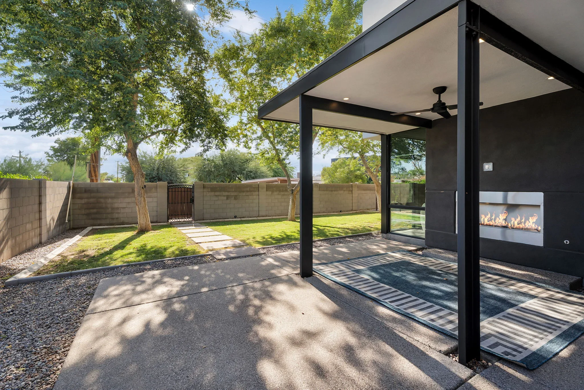 Black steel patio structure with fireplace, concrete paving, and manicured lawn