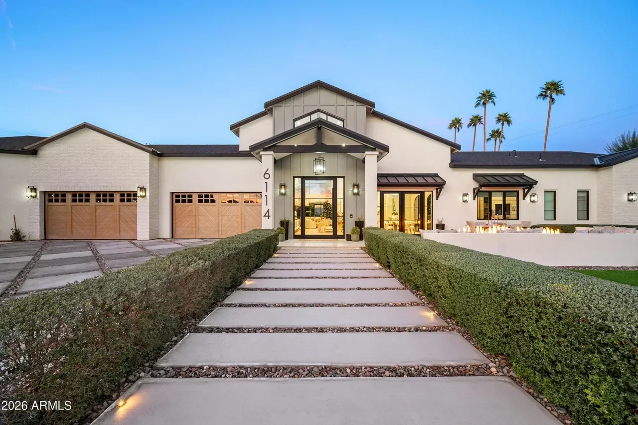 White brick farmhouse with wood garage doors, concrete driveway, and landscaped hedges