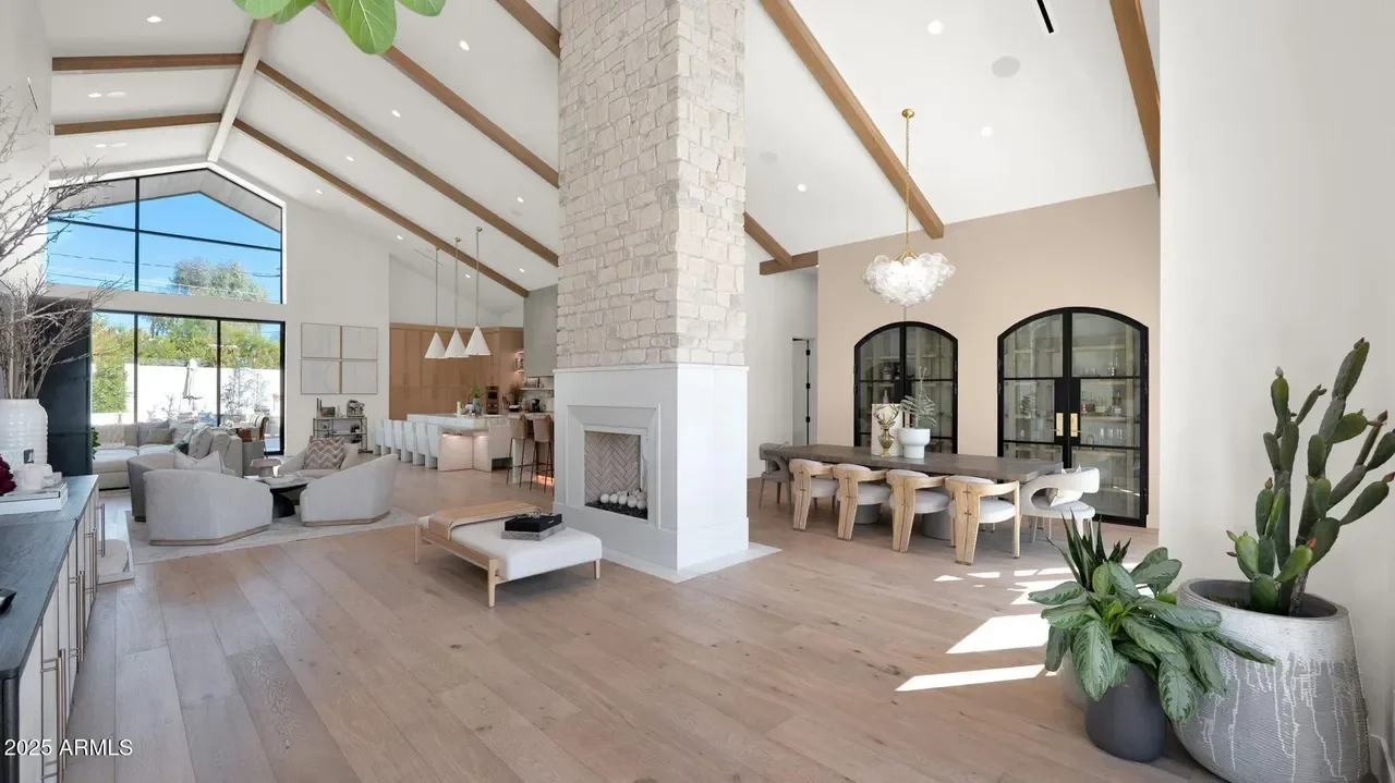 Open-concept living space with exposed wood beams, fireplace, and arched glass doors