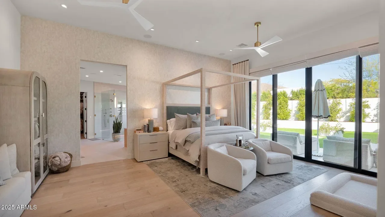 Modern primary bedroom with canopy bed, wood floors, and ensuite bathroom with glass shower