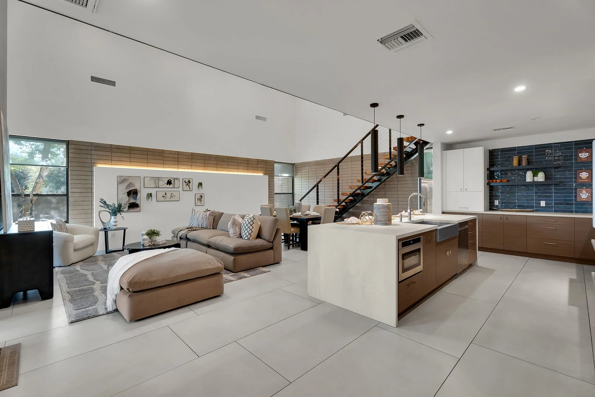 Open concept living space with light tile flooring, wood cabinetry, white quartz island, and modern staircase