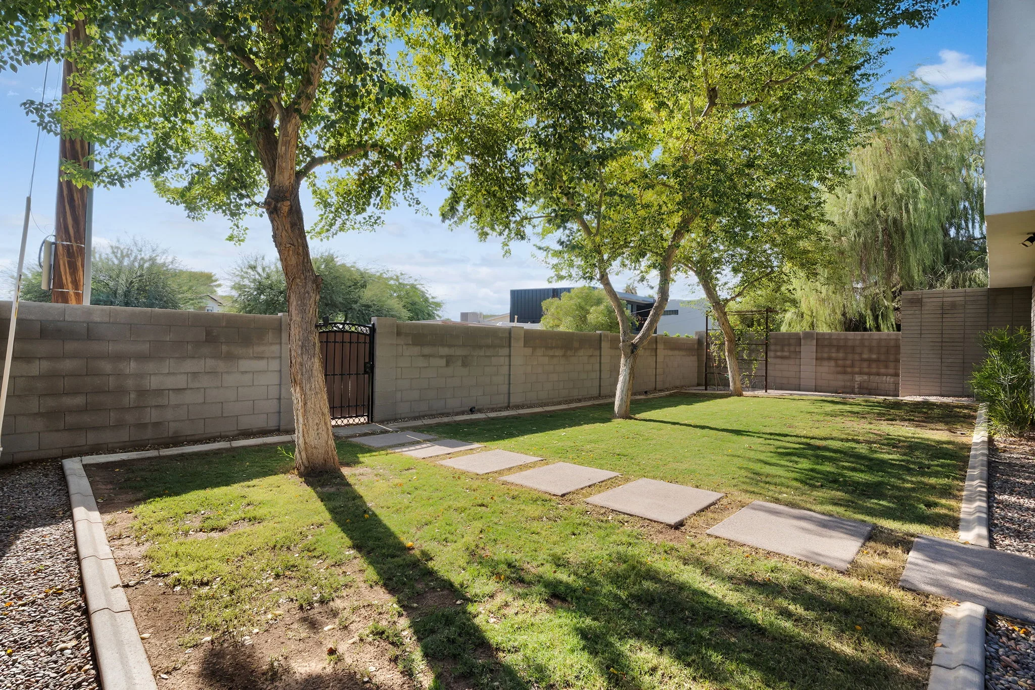 Concrete block fence with stepping stones, mature trees, and new lawn in residential backyard
