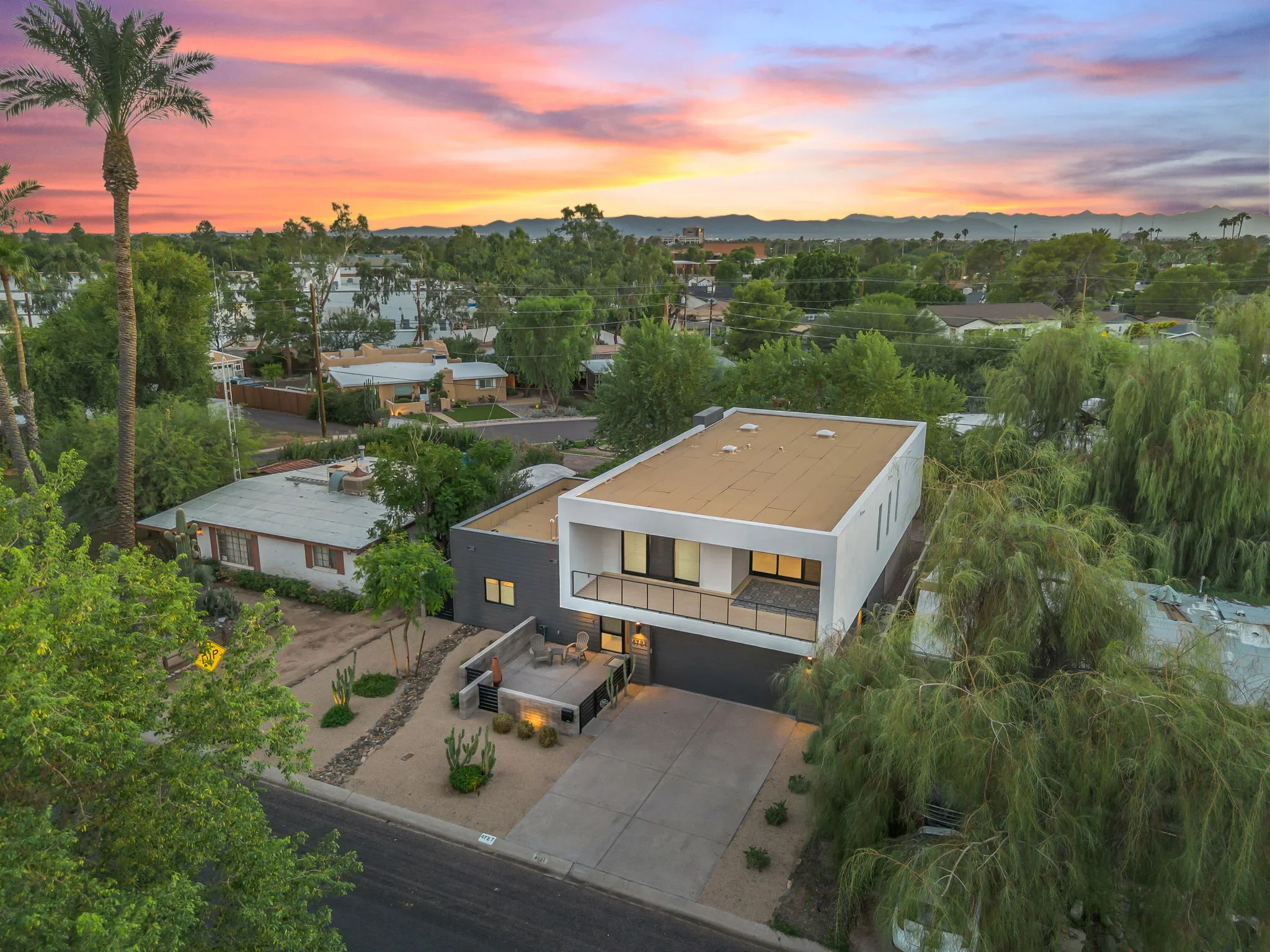Modern two-story home with white and dark exterior, flat roof, concrete driveway, and desert landscaping