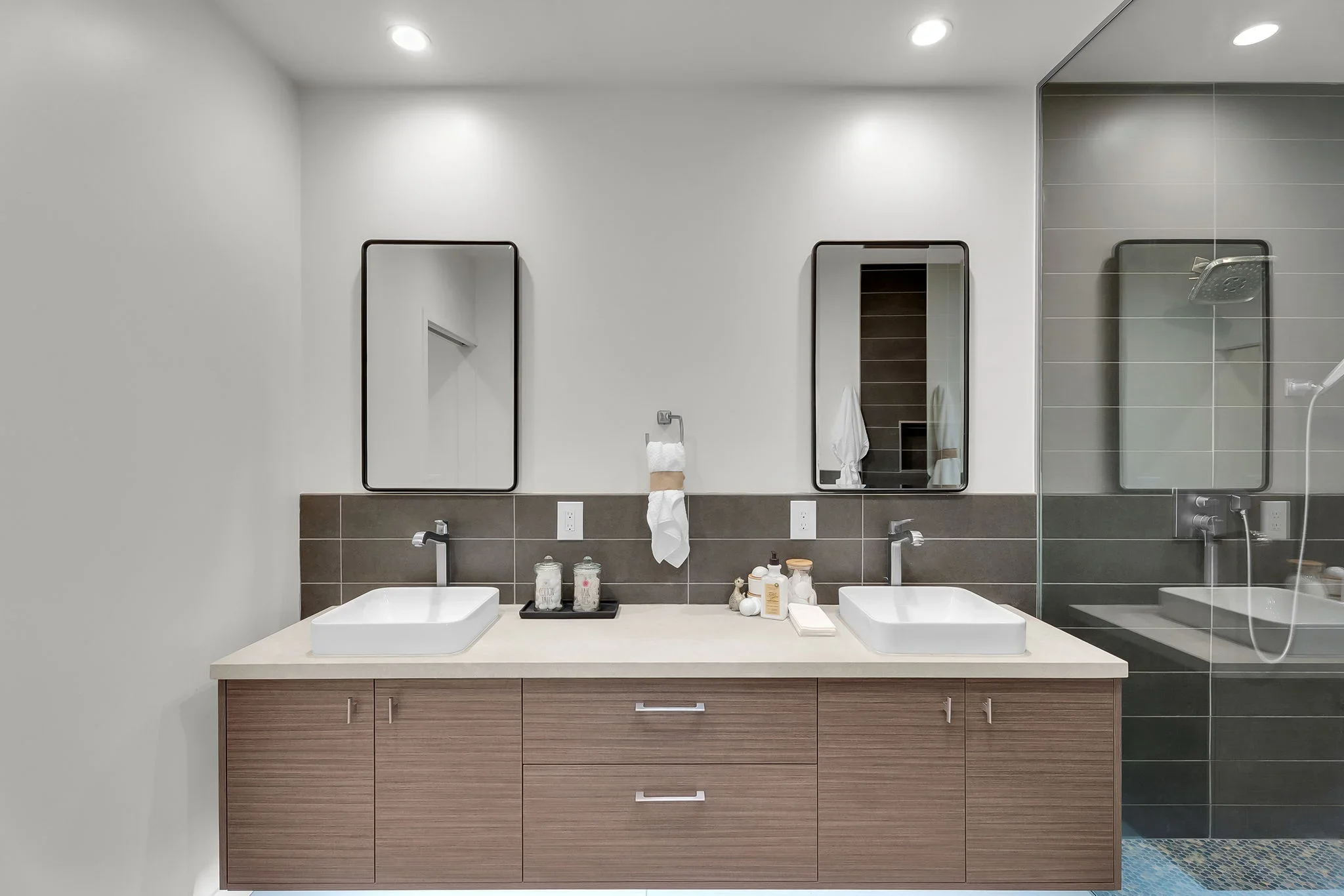 Dual-sink bathroom vanity with wood cabinetry, quartz countertop, vessel sinks, and glass shower enclosure