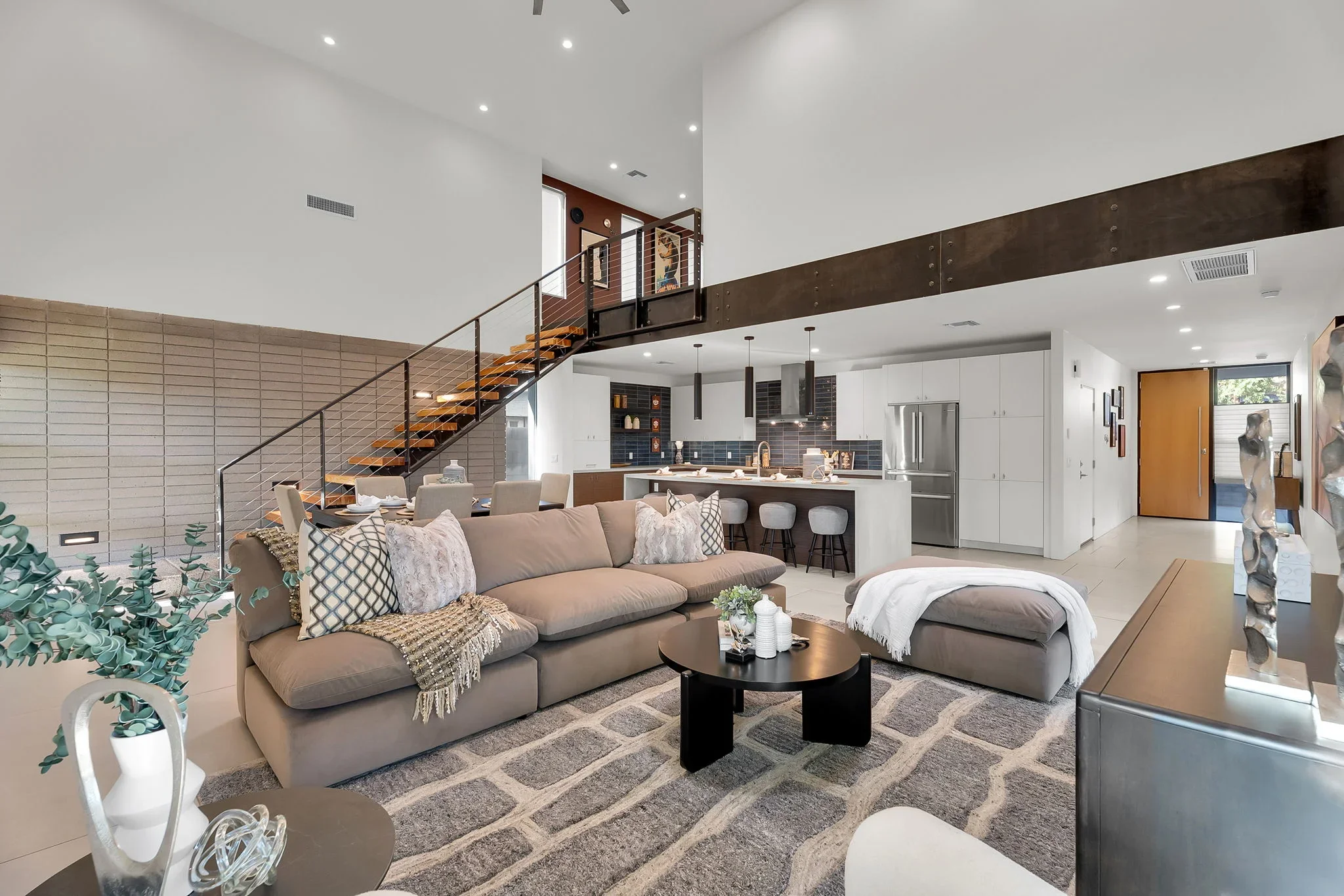 Open-concept living space with steel beam, wood staircase, white walls, and modern kitchen with stainless steel appliances