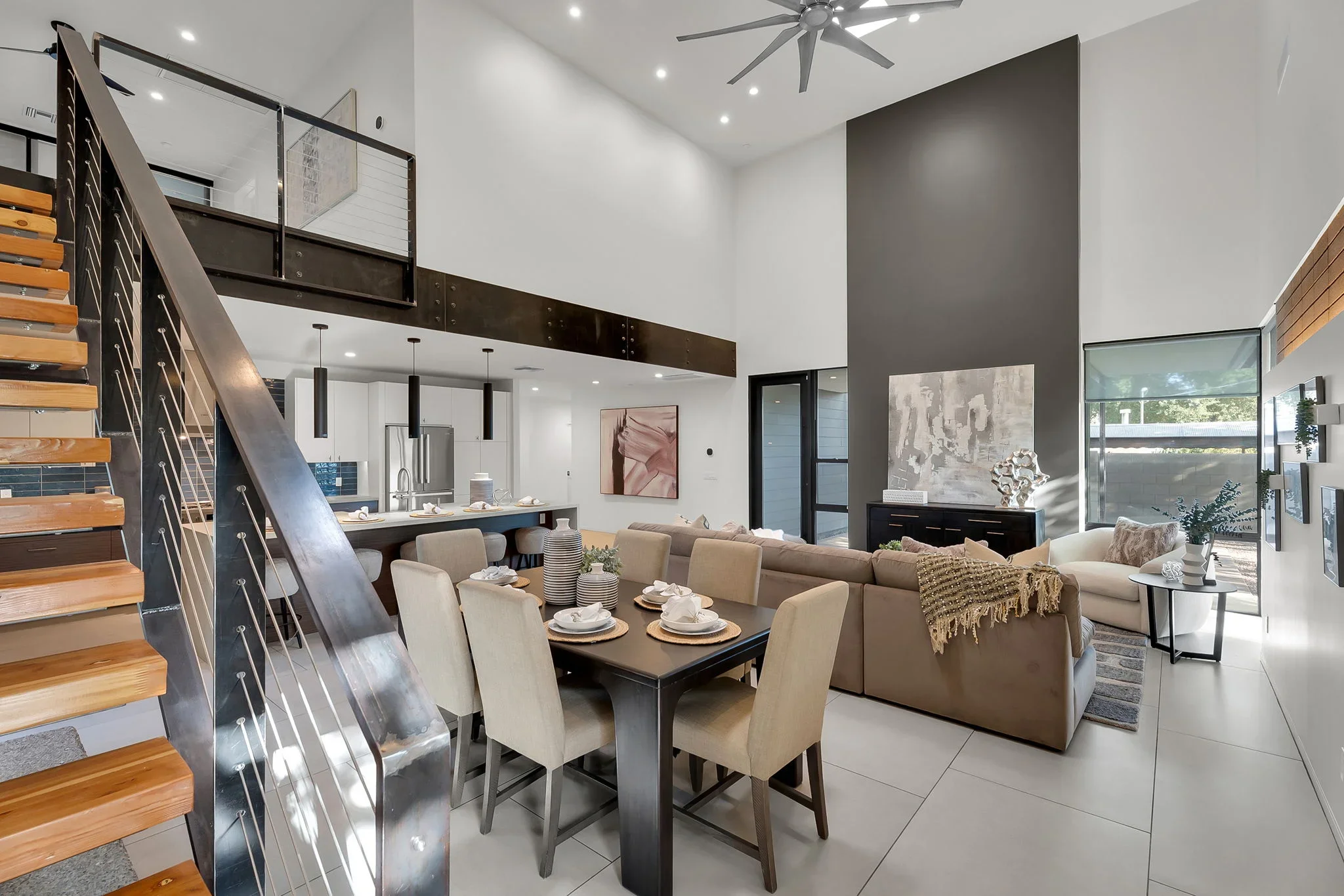 Open-concept living space with floating loft, steel staircase, white walls, gray accent wall, and modern kitchen
