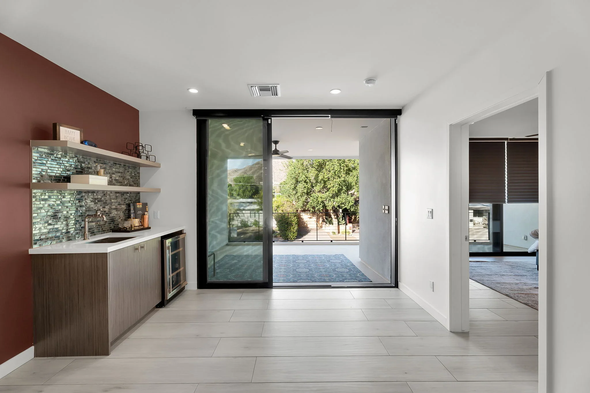 Modern kitchen with wood cabinetry, glass tile backsplash, and black-framed sliding glass doors to patio