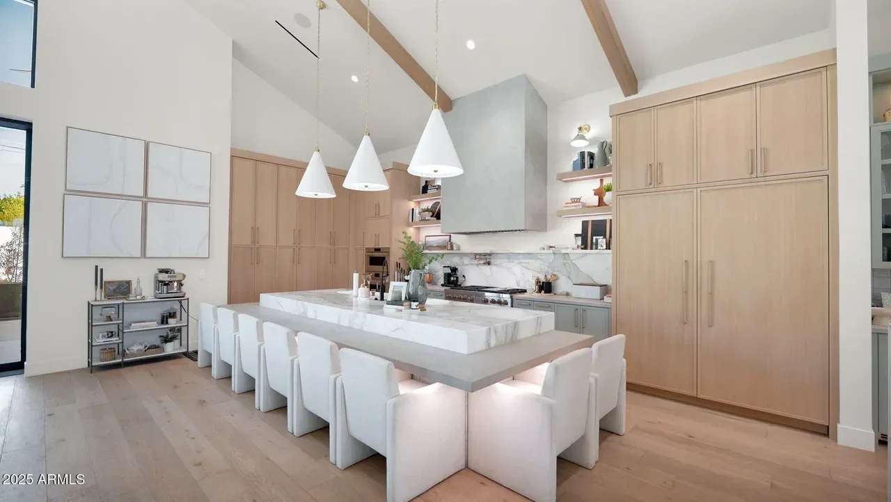 Modern kitchen with light wood cabinets, marble island, white pendant lights, and vaulted ceiling