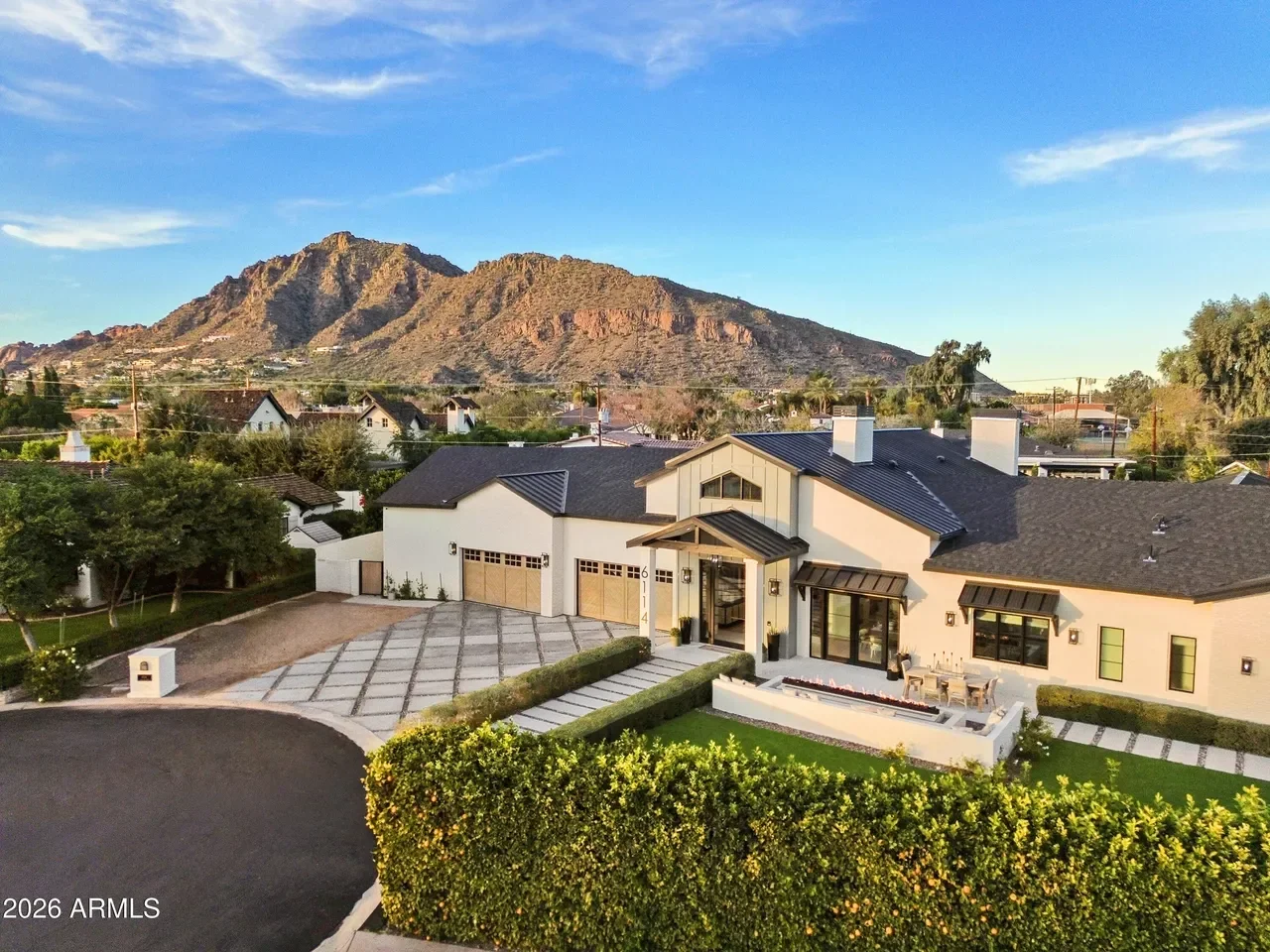 Contemporary stucco home with dark metal roof, three-car garage, and geometric paver driveway